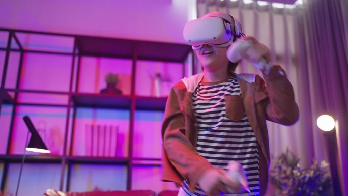 隔离期内，亚洲男童戴着VR或虚拟现实眼镜，戴着耳机，站在起居室电视机前玩视频游戏