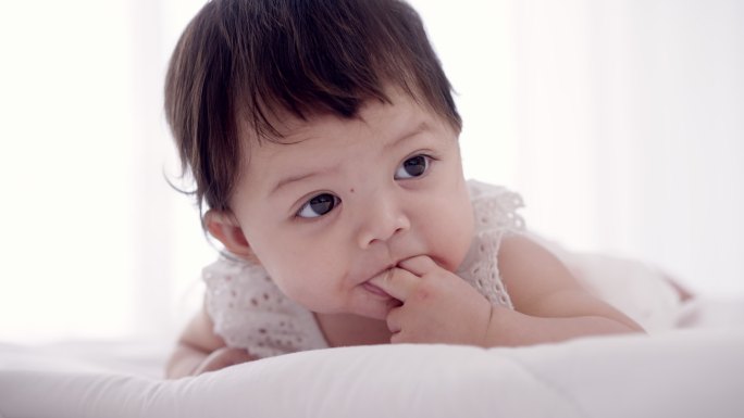 天真可爱的亚洲小女婴开心地吮吸着手指的特写镜头。妈妈用尿布擦去小女儿脸上的唾液。