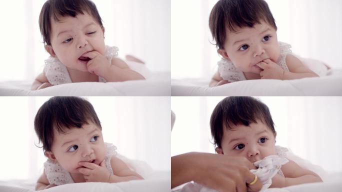 天真可爱的亚洲小女婴开心地吮吸着手指的特写镜头。妈妈用尿布擦去小女儿脸上的唾液。