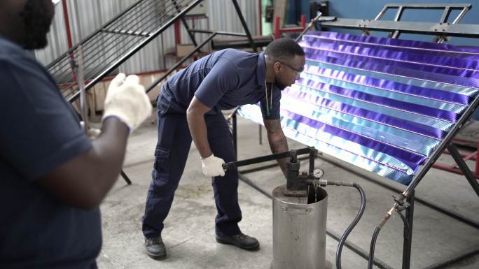 在太阳能电池板工厂，非裔美国人主管监督工人将水泵入电池板进行测试