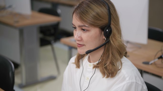 POV：微笑的亚洲女性，戴着耳机，使用笔记本电脑，在办公室与客户支持服务运营商交谈
