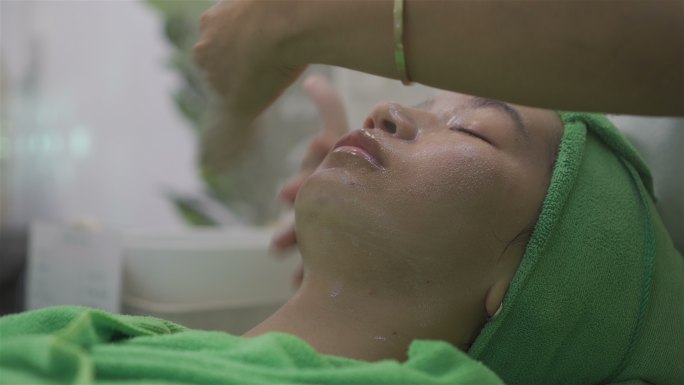 年轻的亚洲女孩躺在床上进行面部按摩水疗