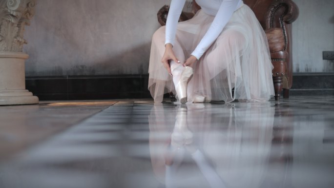 美丽的年轻芭蕾舞演员在演播室的地板上系鞋，鞋上系着丝带