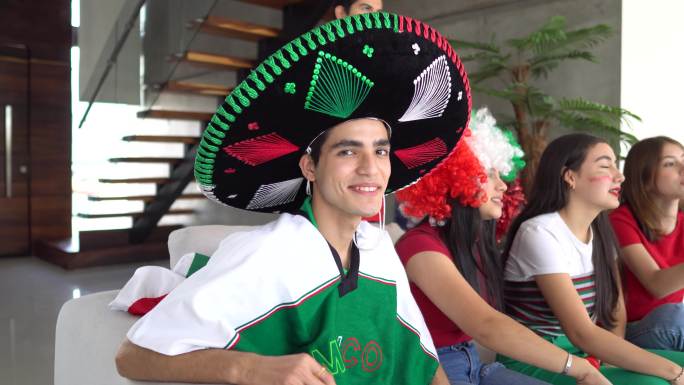 一个十几岁的拉丁男孩与朋友在家观看墨西哥足球队比赛的照片