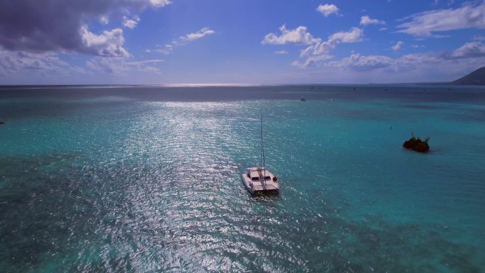 波光粼粼的海面上双体帆船与美丽珊瑚岛礁