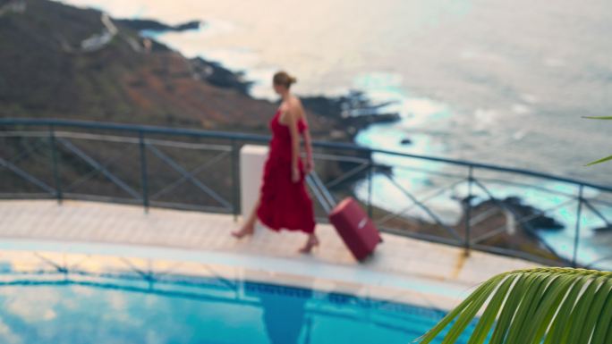 游泳池女神到来。穿着红色连衣裙，提着手提箱沿着边缘行走