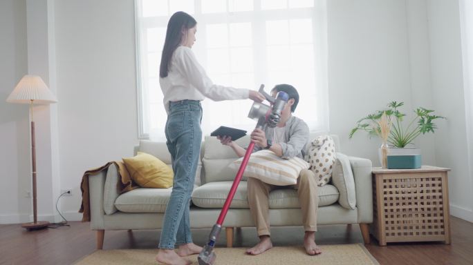 一对亚洲夫妇用吸尘器清洁起居室，这是一种人性化和家务化的概念