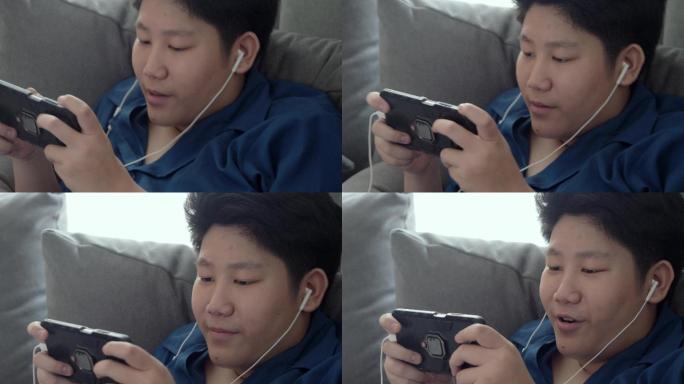 快乐的亚洲男孩在家里靠窗的沙发上玩手机游戏，生活方式理念。