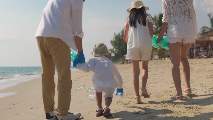 快乐亚洲大家庭与垃圾袋一起清理海滩上的区域。