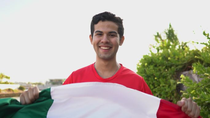 一个十几岁的拉丁男孩在户外举着墨西哥国旗的肖像