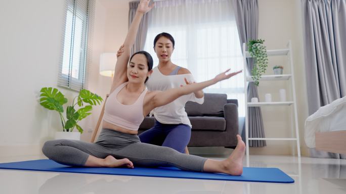 亚洲家庭健身女教练教苗条美丽的亚洲女性练习瑜伽，手臂向上抬起，上身尽可能向左倾斜，在客厅的垫子上伸展