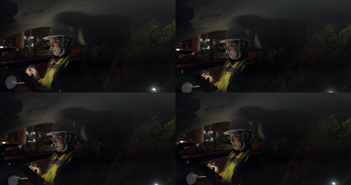 亚洲土木工程师男子戴安全帽，穿安全背心在工地上夜班。工头坐在车上，在数字平板上检查结构的进度，并在城