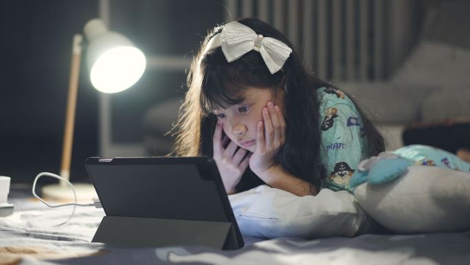 小女孩晚上在卧室使用数字平板电脑