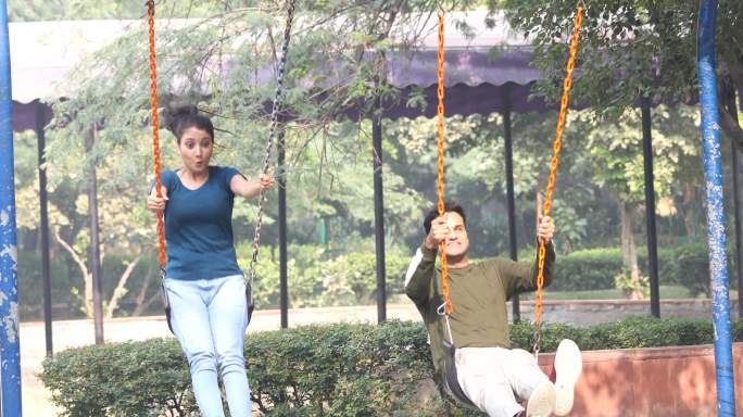 一对年轻夫妇在公园里坐在秋千上，双臂伸开