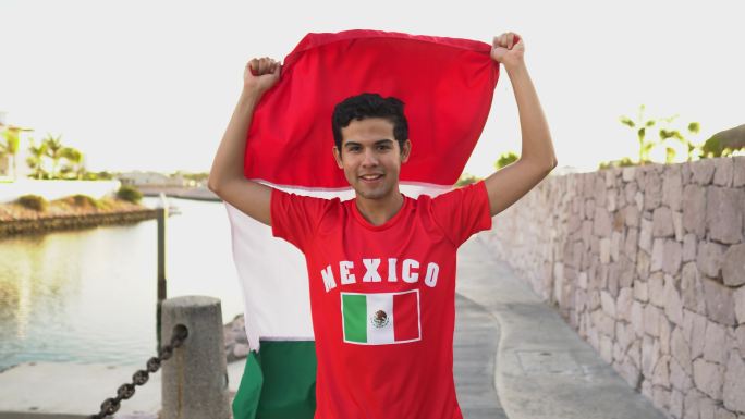 一个十几岁的拉丁男孩在户外行走并举着墨西哥国旗的肖像