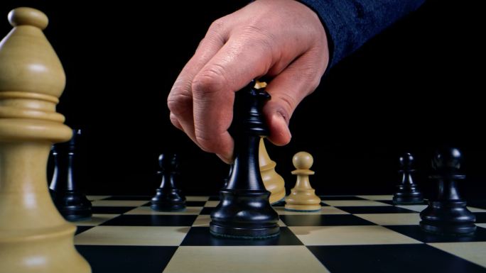 在国际象棋比赛中，一只白人男性手拿着一个白人皇后和他的黑人皇后