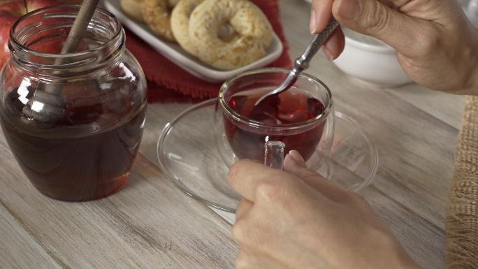 白色乡村桌子上，一位女士双手在杯中搅拌芙蓉热茶的高角度特写镜头