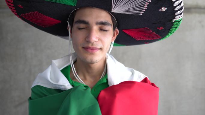 一个十几岁的拉丁男孩举着墨西哥国旗，头戴草帽
