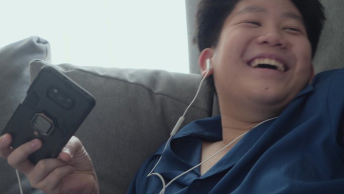 快乐的亚洲男孩在家里靠窗的沙发上玩手机游戏，生活方式理念。