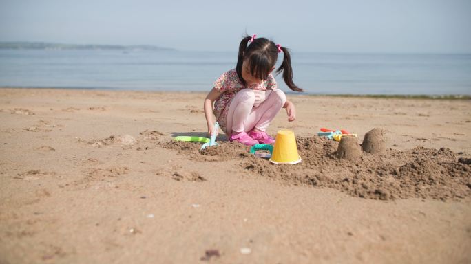 年轻女孩在夏日海滩上建造金沙城堡