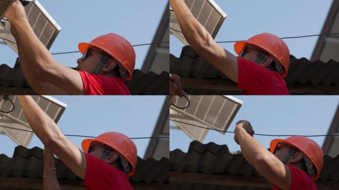 亚洲男子用钻头将太阳能电池板安装到金属基座上。在一个阳光明媚的日子里，他在屋顶上工作。