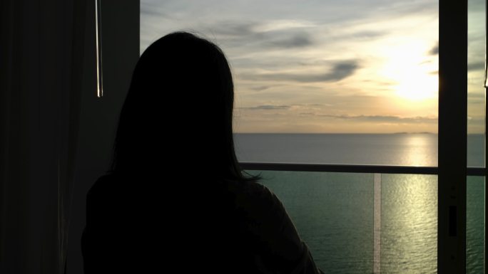 剪影女子在海上度假室打开窗帘看日落
