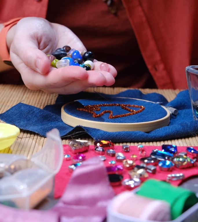 坐在书桌旁，在家里制作珠子和水晶首饰的成熟女性的双手