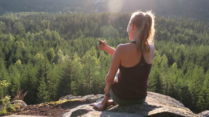 年轻女子在山谷边俯瞰的岩石山顶上休息