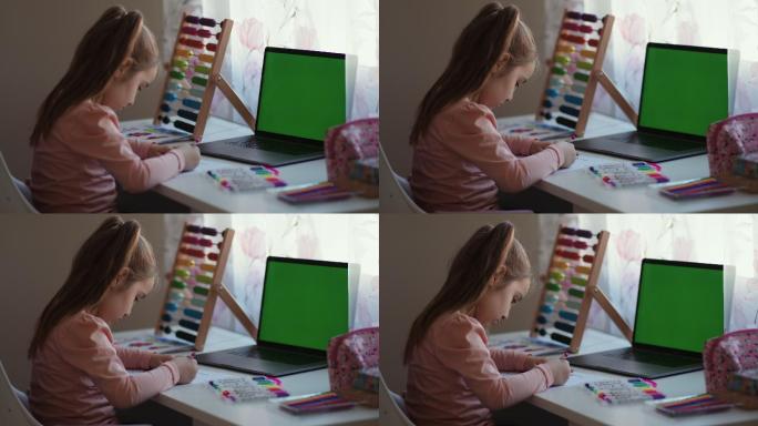 小女孩正坐在桌旁，用带有色度关键技术绿色屏幕的笔记本电脑画画