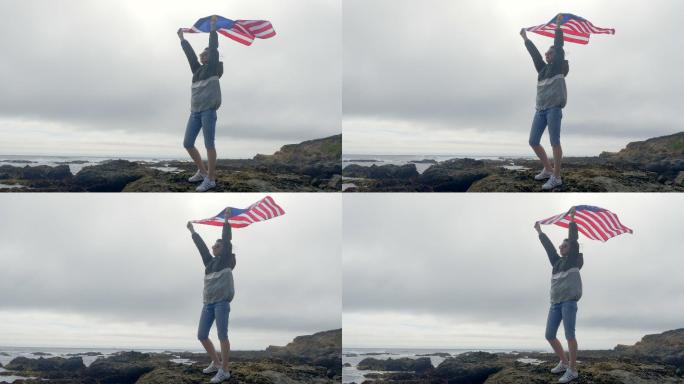 太平洋野生海岸岩石上挂着美国国旗的女人。加利福尼亚