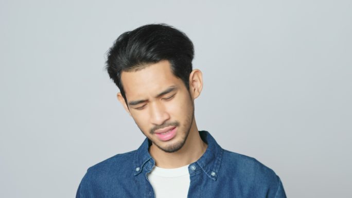 照片中，一名年轻的亚洲男子站在工作室的灰色背景上，脸上流露出失望的表情，分辨率为4k