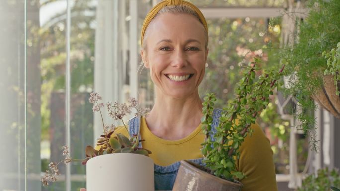 成熟的高加索女性花商在苗圃外捧着植物微笑