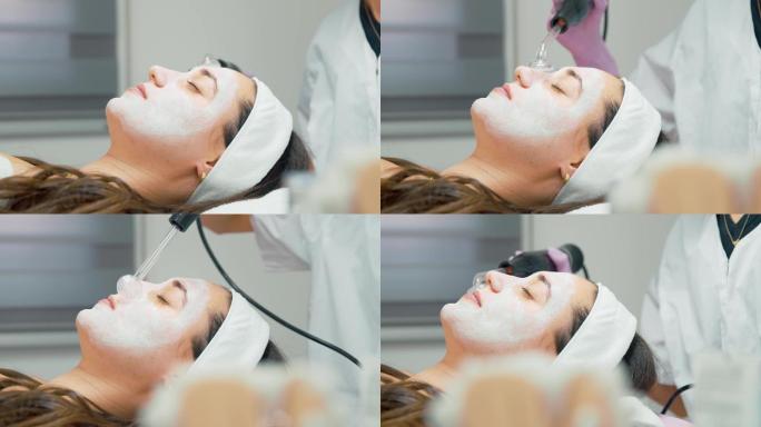 女客户涂有奶油的脸躺在床上，专家在医务室的头顶和鼻孔上使用高频d'arsonval设备