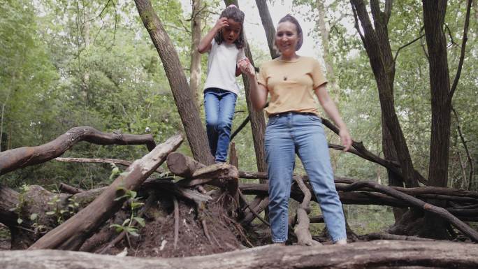 母亲在森林里帮助女儿在倒下的树枝上行走