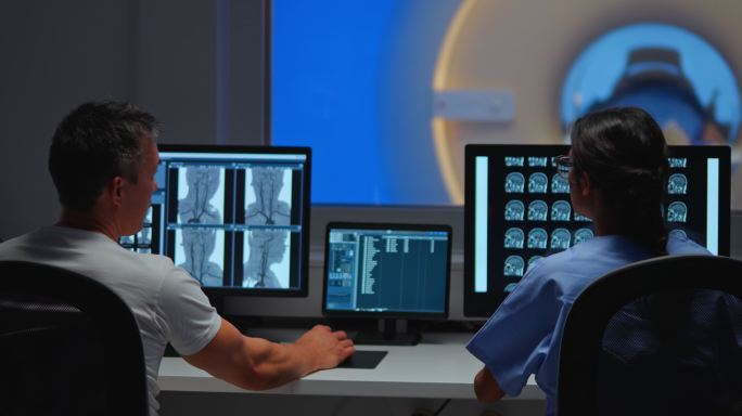 两名放射科医生在控制室的计算机屏幕上查看MRI图像