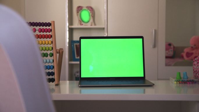 学校用品。儿童房桌子上的笔记本电脑显示绿色彩色按键屏幕的场景。技术背景概念