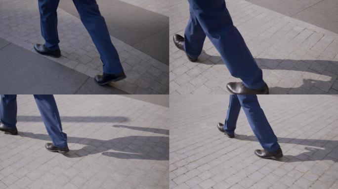 摄像机特写了一个行走的商人的腿。这位商人穿着蓝色西装，脚上穿着经典的棕色鞋子。夏天，一个商人在街上沿