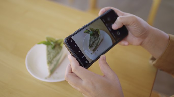 咖啡馆桌上的绿茶蛋糕和手用手机拍照