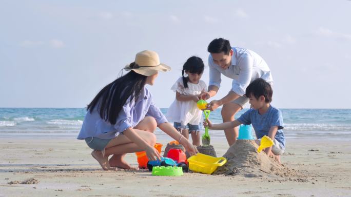 幸福的一家，父亲是亚洲人，母亲是4-8岁的男孩和女孩，他们在夏天的海滩上玩沙滩玩具。积极的家长和人们