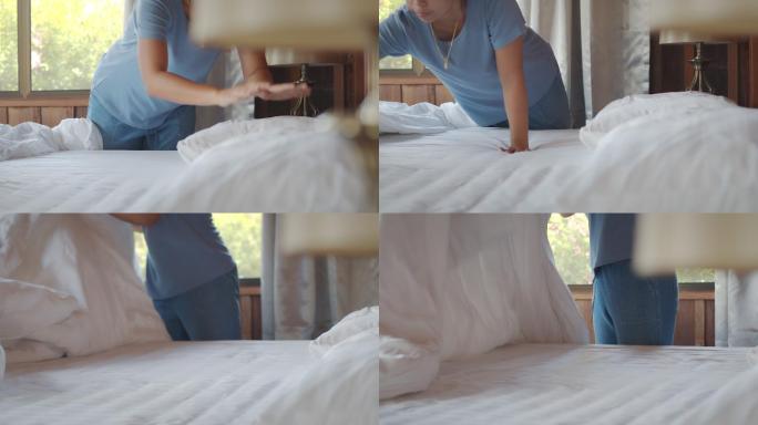 一位亚洲女性早上醒来后，在卧室里整理毯子和被褥。