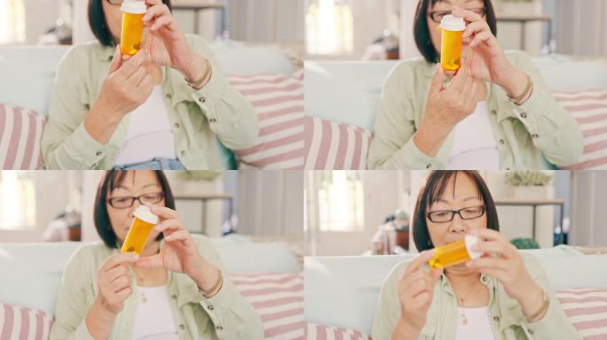 一位亚洲老妇人独自坐在家里，看着一瓶药丸。生病的亚洲老妇人在家的客厅里拿着药
