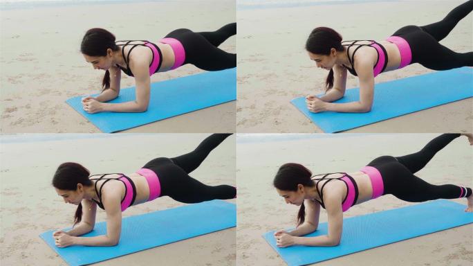 在瑜伽垫上做瑜伽板姿势的女人。早上，亚洲女性在海天多云的海滩上穿着运动服。