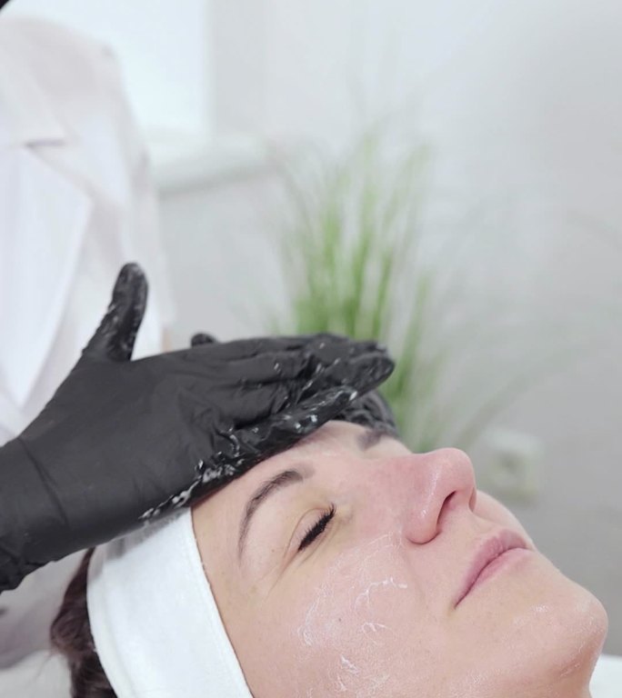 美容师用化妆品滋润女性面部皮肤。