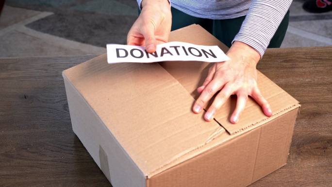 一个面目全非的人正在往一个盒子里装食物，以捐赠给需要帮助的人