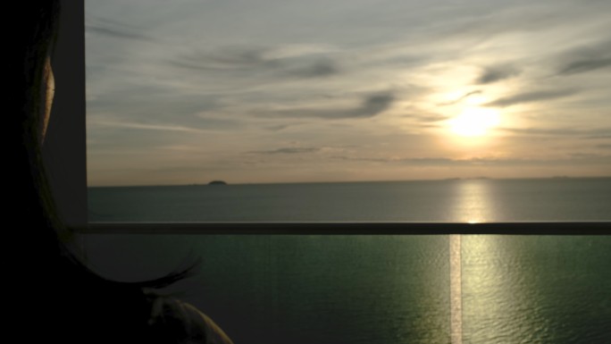 剪影女子在海上度假室打开窗帘看日落