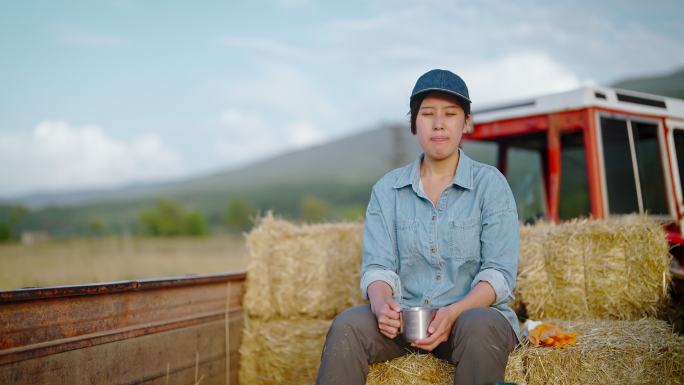 年轻的女农民坐在干草堆上的拖拉机拖车上，在农田里休息