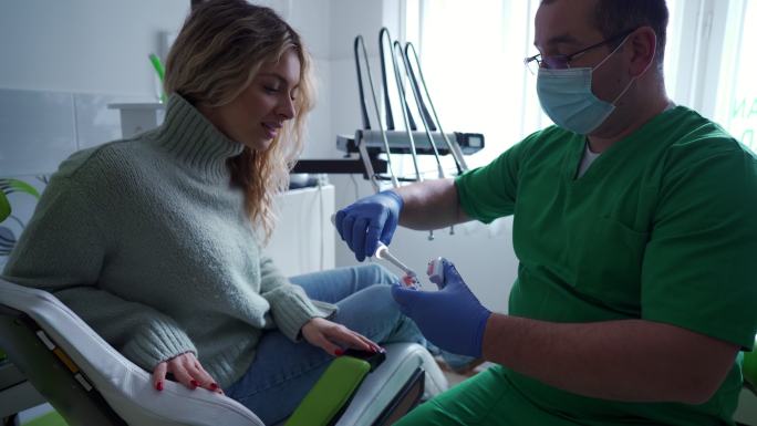 男牙医使用模型教女患者如何正确刷牙