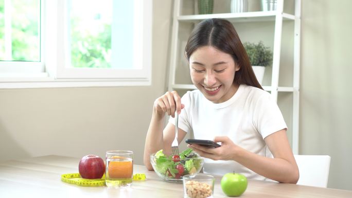 美女吃健康蔬菜沙拉，用智能手机。