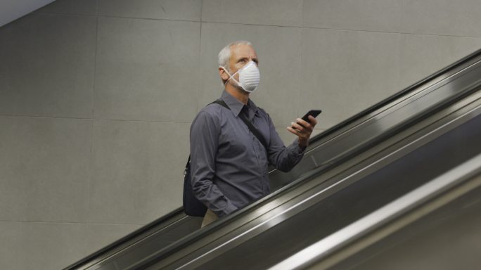 一名白人男子戴着抗击冠状病毒的面罩在地铁站内走动