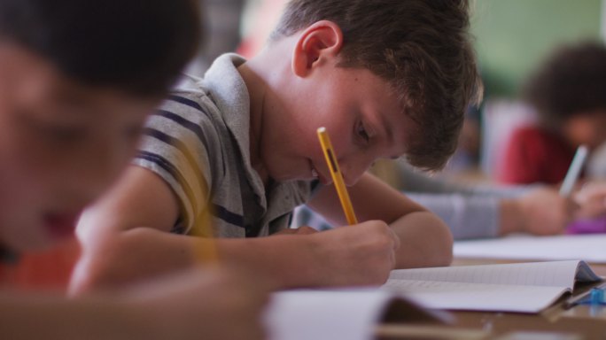 两个男孩在学校坐在他们的桌子上写作